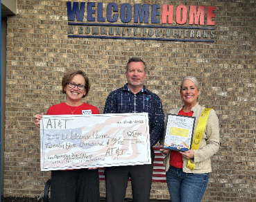 woman in red and man in dark shirt holding large check from AT&T to welcome home for $25,000